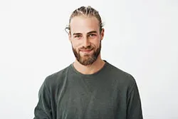 Młody mężczyna w blond włosach związanych w kucyk.